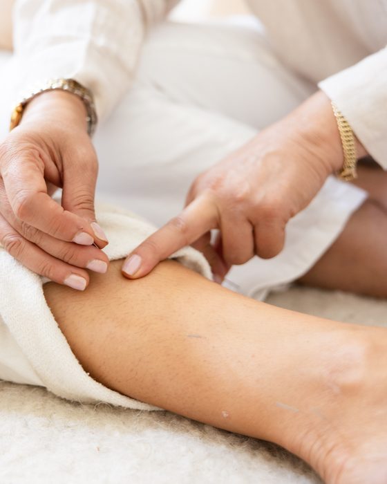 Close detail of Vida's hands placing an acupuncture needle at a patient's knee.